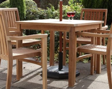 A square teak outdoor dining table and four stacking armchairs around it on a patio