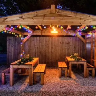 A wooden gazebo with waterproof roof at night time with colourful christmas lights