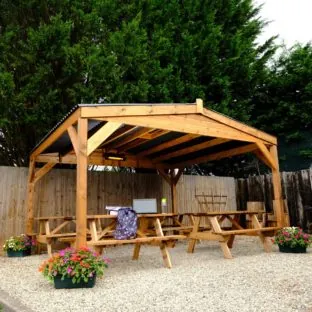 A rectangular wooden gazebo with a bitumen composite roof with 4 picnic tables underneath it