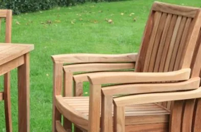 A stack of 3 teak outdoor chairs next to a square teak outdoor table on a patio